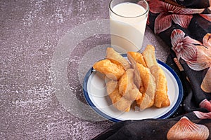 Deep-fried dough sticks on white plate and a glass of soybean milk on gray stone background