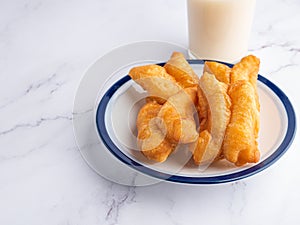 Deep-fried dough sticks on white plate and a glass of soybean milk on marble table