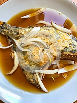 deep-fried flounder with onions and vegetables in Asian sauce on a plate.