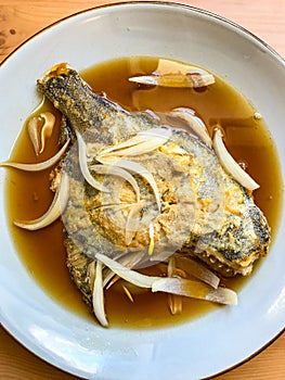 deep-fried flounder with onions and vegetables in Asian sauce on a plate.