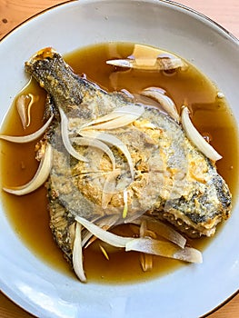 deep-fried flounder with onions and vegetables in Asian sauce on a plate.