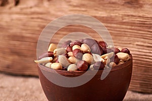 Deep fried peanuts in clay bowl over rustic wicker background. Selective focus
