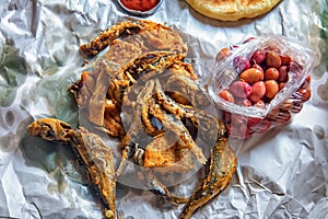 Deep fried sardine lies on oiled paper and near lies pickled olives