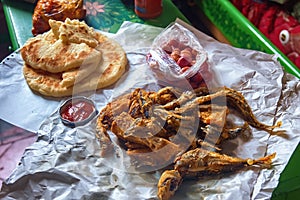 Deep fried sardine lies on oiled paper and near lies pickled olives, tomato sauce and flatbread