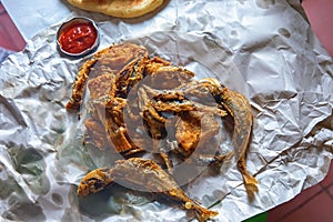 Deep fried sardine lies on oiled paper and near lies tomato sauce