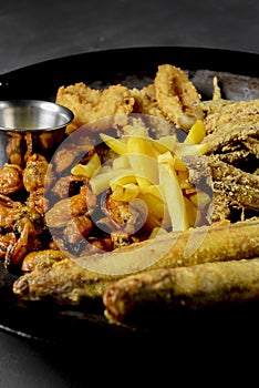 Deep fried set made from french fries, onion rings, big and small fried fish served in a wok over black background.