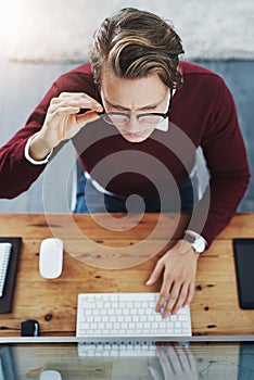 Deep in the make it happen zone. High angle shot of a young man using a computer at his desk in a modern office.