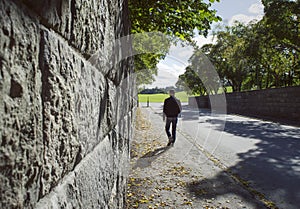 Deep perspective along a stone wall and a man walking in an autumn street.