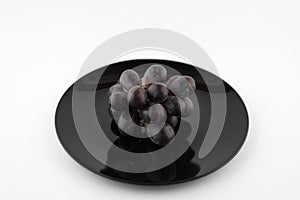 Deep red bunch of grapes on black plate, isolated on white background