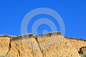 Deep sandy cliff on the background of blue sky.