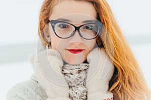 Deep sight of the attractive red head woman wearing glasses. Time-spending in the countryside during the snowfall.