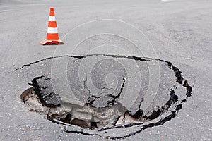 Deep sinkhole on street city and orange traffic cone. Dangerous hole in asphalt highway. Road with crack. Damaged surface collapse