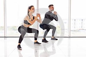 Deep squat. Fitness couple in sportswear doing squat exercises at gym