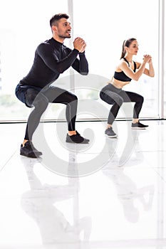 Deep squat. Fitness couple in sportswear doing squat exercises at gym