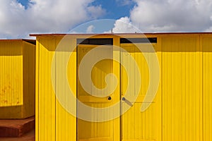 Deep yellow painted beach huts, on sunny but moody day. Blue sky, white clouds, seaside holiday architecture.