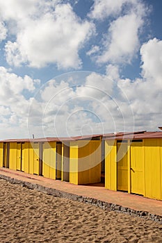 Deep yellow painted beach huts, on sunny but moody day. Blue sky, white clouds, seaside holiday architecture.