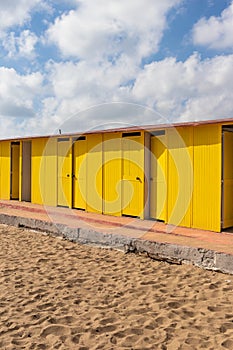 Deep yellow painted beach huts, on sunny but moody day. Blue sky, white clouds, seaside holiday architecture.