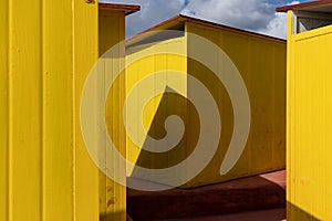Deep yellow painted beach huts, on sunny but moody day. Blue sky, white clouds, seaside holiday architecture.