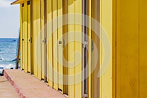 Deep yellow painted beach huts, on sunny but moody day. Blue sky, white clouds, seaside holiday architecture.