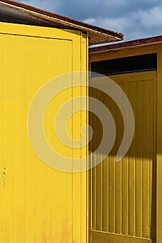 Deep yellow painted beach huts, on sunny but moody day. Blue sky, white clouds, seaside holiday architecture.