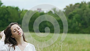 Deeply relaxed woman in green field touches her hair with eyes closed oneness
