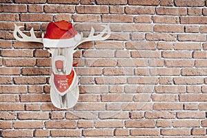 Deer hanging on the brick wall with a Santa Claus cap and red necklace