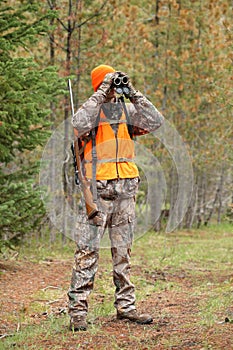 Deer hunter in woods looking through binoculars
