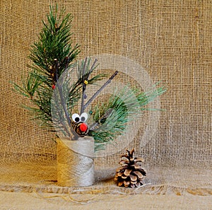 Deer made of cones and twigs decorated with bells on jute reel with green pine branches and cone on homespun cloth. Handmade.