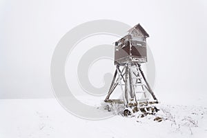 Deer stand, wooden hunters high seat hide on snow covered field, winter day