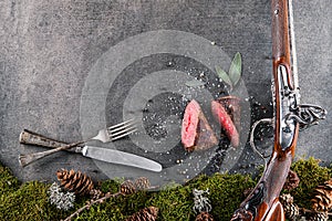 Deer or venison steak with antique long gun, cutlery and ingredients like sea salt, herbs and pepper, food background for restaura