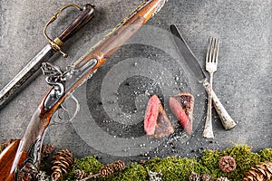 Deer or venison steak with antique long gun, cutlery and ingredients like sea salt and pepper, food background for restaurant or h