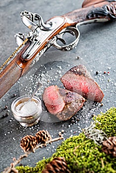 Deer or venison steak with antique long gun and ingredients like sea salt and pepper, food background for restaurant or hunting lo