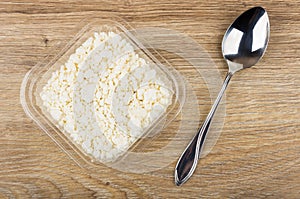 Defatted cottage cheese in plastic box and spoon on table