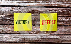 Defeat vs Victory words written on old paper on yellow background.