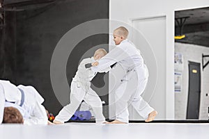 Defense. Boys, children in white kimono training, practising judo, jiu-jitsu exercises indoors. Professional sport
