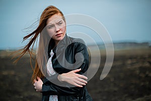 A defenseless sweet girl stands in the cold wind and hugs herself.