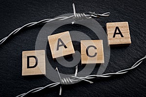 Deferred action for child arrivals concept with barb wire next to letters that spell the acronym DACA. DACA is a piece of