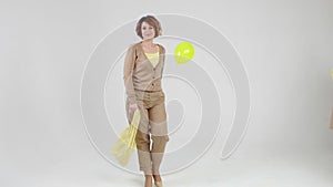 Defile of young woman with yellow balloon in hand is walking in trousers and blouse on light background.