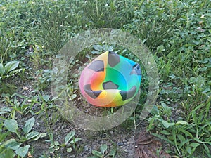 Deflated multicolored soccer ball on dirt and grass