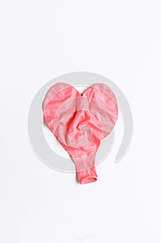 Deflated wrinkled pink heart shaped balloon laying flat on white background