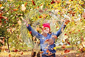 Defocus autumn people. Teen girl raising hand and throwing leaves. Many flying orange, yellow, green dry leaves. Joy