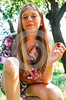 Defocus beautiful smiling teenage girl in dress sitting against green summer background. Teen girl holding raspberries