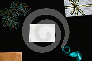 Defocus blank white card with fir tree branch, gift bow, craft envelope and blue ribbon on black background. Frame