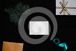 Defocus blank white card with spruce tree branch, gift bow, craft envelope and blue ribbon on black background. Frame