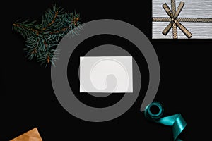 Defocus blank white card with spruce tree branch, gift box, craft envelope and blue ribbon on black background. Frame