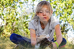 Defocus blonde little expression girl playing and caress cat, black and white small kitten. Nature blurred green summer