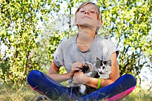 Defocus blonde little girl caress cat, black and white small kitten. Nature green summer background. Girl holding and