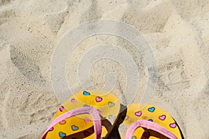 Defocus bright yellow and pink slippers flip flops with pink and blue hearts on the sand. Summer background.The concept