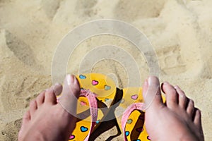 Defocus dirty bright yellow and pink slippers flip flops with hearts on the sand. Blurred female feat. Summer background