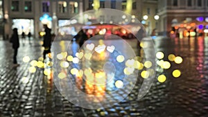 Defocus  evening rainy street blurred light house vitrines reflection on wet pavement people walking with umbrellas medieval city